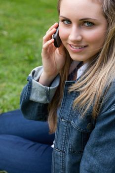 Young smiling girl using her mobile phone while sitting down in the countryside