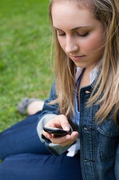 Young girl sending a text with her cellphone while sitting on the grass in a park