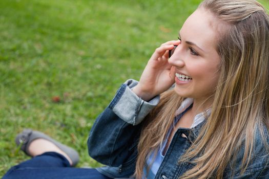 Young happy blonde girl calling with her mobile phone while sitting in the countryside