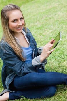 Young happy girl looking at the camera while touching her tablet pc in a parkland
