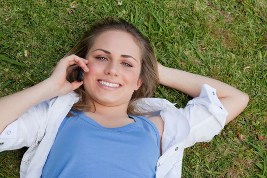 Young smiling blonde girl lying on her back in a parkland while looking up