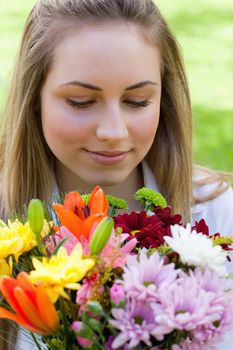 Young relaxed blonde girl smelling a beautiful bunch of flowers while closing her eyes