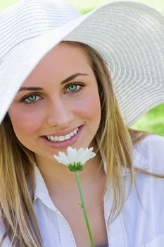 Young pretty blonde girl wearing a hat while holding a white flower in a parkland