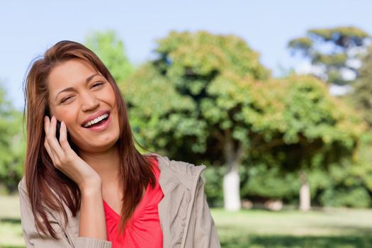 Young woman laughing joyfully while on the phone in a bright grassland  area