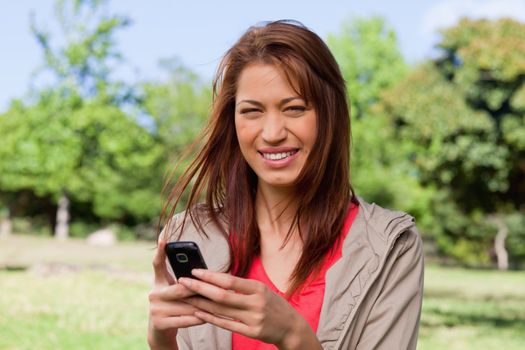 Young woman with a gleeful expression holding a phone in a park on a sunny day