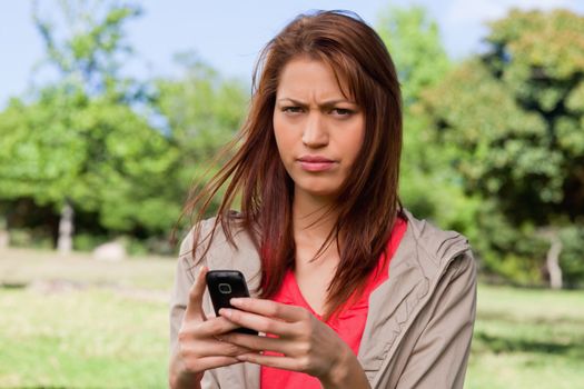 Young woman with a serious expression holding a phone in a sunny park