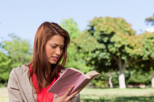 Woman with a ambitious expression on her face reading a book in a sunny area surrounded by trees