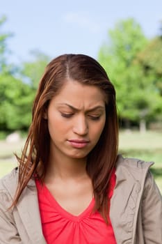 Woman looking towards the ground with a disappointed expresssion on her face in a sunny park