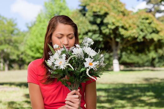 Young woman smelling a bunch of flowers while standing in a bright grassland area