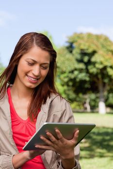 Young woman smiling while using a tablet and standing in bright park