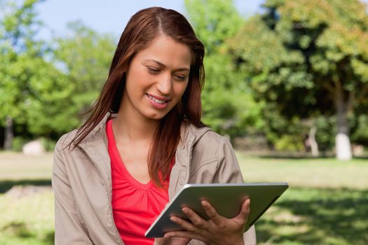 Woman leaning her head to the side while smiling and using a tablet in a bright park
