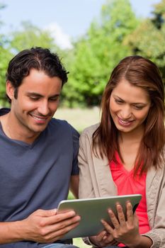 Man and his friend smiling as the watch something on a tablet in a sunny park