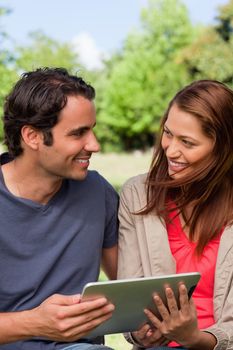 A man and a woman happily look at each other while they are holding a tablet in a bright park