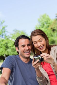 Two friends smiling happily as the look at the photo collection in a camera while sitting in a sunny park