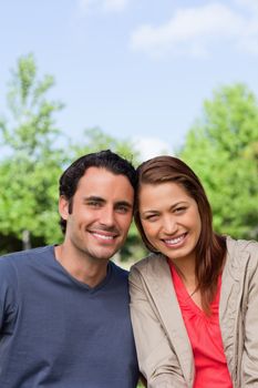 Two friends smiling as the look ahead while sitting side by side in a bright park environment