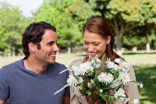 Woman joyfully looking at a bunch flowers as she is being watched by her friend who is smiling in an open grassland area