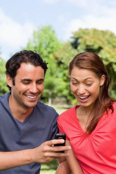 Woman excitedly watches as she is shown something on the friend's mobile phone while sitting in an open park area