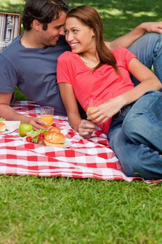 Two friends looking into each others eyes while resting their heads together as they lie on a blanket with a picnic basket and food