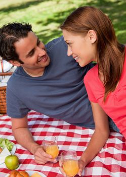 Close-up of two smiling friends looking into each others eyes while they hold glasses as they lie on a blanket with a picnic