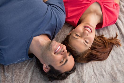 Two smiling friends lying next to each other as they look into the sky while on a grey quilt