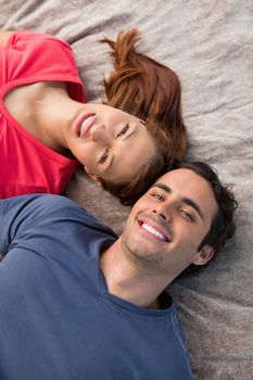 Close-up of two smiling friends lying next to each other as they look into the sky while on a grey quilt