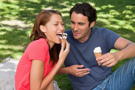 Woman eating ice cream while sitting with her smiilng friend on grass