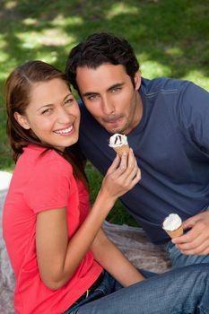 Two smiling friends looking towards the sky while holding ice cream and sitting on grass