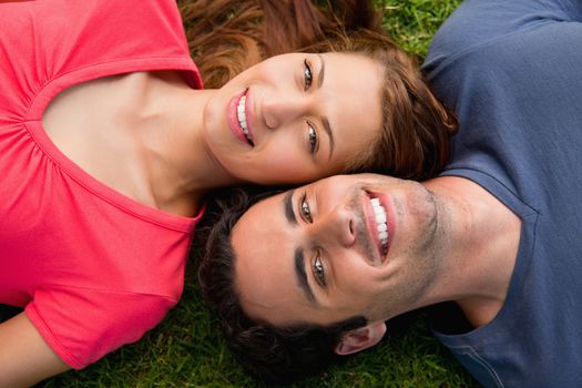 Two friends smiling while lying head to shoulder on the grass