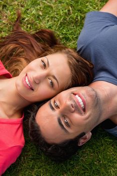 Close-up of two friends smiling while lying head to shoulder on the grass