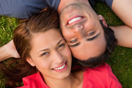 Close-up of two friends smiling while looking towards they sky as they lie head to shoulder with an arm behind their head on the grass