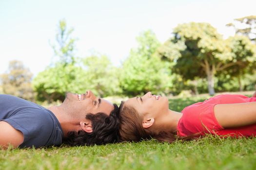 Two smiling friends looking upwards while lying head to head in a grassland area