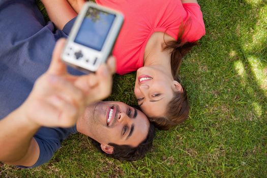 Two smiling friends using a camera while lying side by side on the grass
