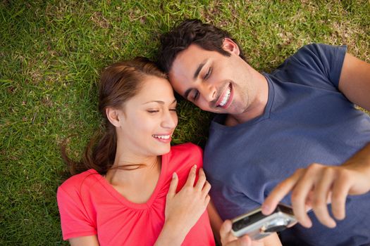 Two friends smiling while looking at photos on a camera as they lie side by side on the grass