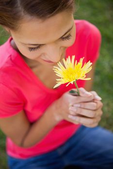 Woman smelling a yellow flower while sitting in the grass