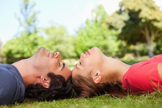 Two friends with their eyes closed as they lie head to head on the grass