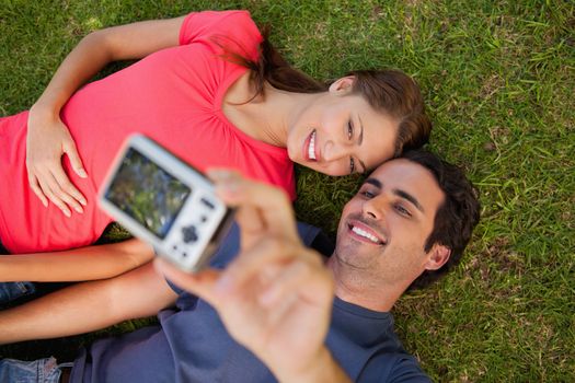 Man taking a photo of him with his friend while lying side by side on the grass