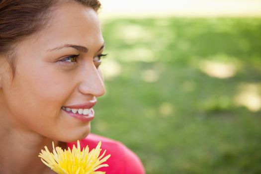Smiling woman looking towards the side while holding a yellow flower with grass in the background