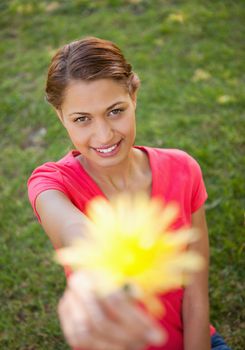 Woman holding a flower in one hand at arms reach with focus on the woman
