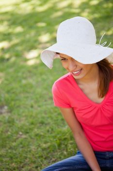 Woman smiling while wearing a white hat as she sits in the grass
