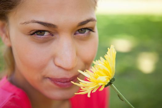 Woman looking upwards while smelling a yellow flower with grass in the background