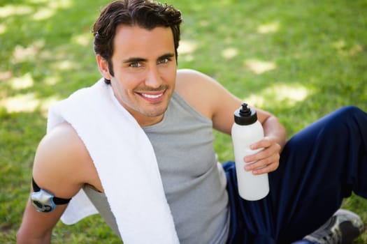 Man smiling with a white towel on his shoulder looking at the camera while holding a sports bottle