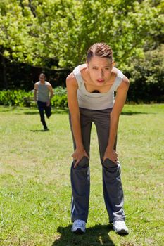 woman bending over to recover while a man is running towards her in the background
