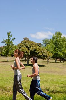 Woman and a man jogging along a running trail with a view of trees and the sky in the background