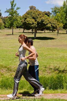 Woman and a man jogging along side each other along a running trail with a view of trees and the sky in the background