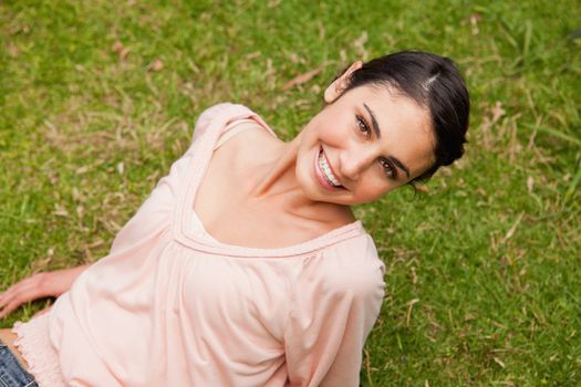 Woman smiling with her head tilted to one side as she lies down on the grass