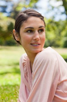 Woman with curious expression on her face looking towards the side as she sits down on the grass