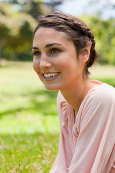 Young woman smiling while looking straight ahead of her while sitting on the grass