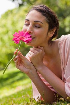 Woman smelling a pink flower with her eyes closed while lying on her front in grass