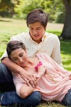 Man smiling as he looks at his friend who is lying against him as he is sitting down on the grass