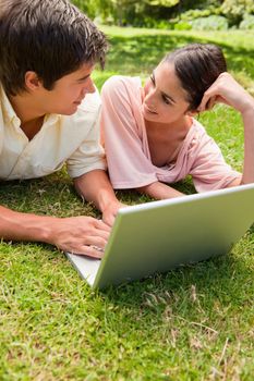 Two friends smiling while looking at each other as they use a laptop together on the grass